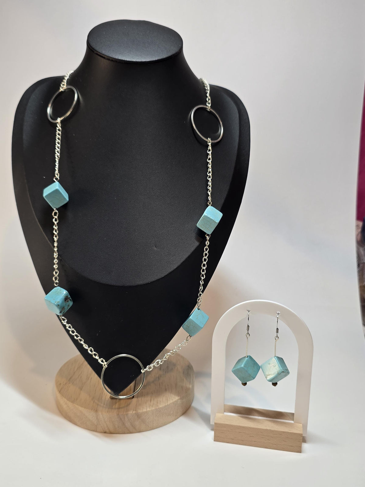 Necklace with turquoise beads on a black mannequin bust, accompanied by matching earrings on a wooden stand.