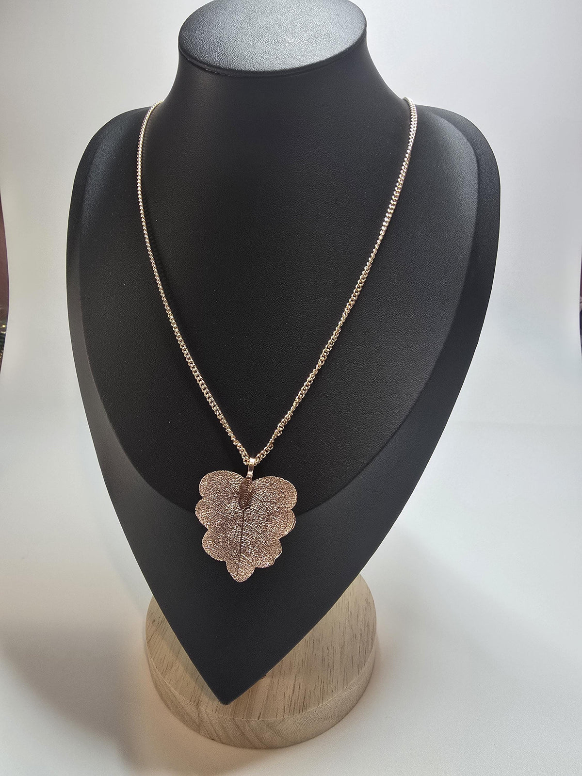 Gold leaf pendant necklace displayed on a black jewelry bust